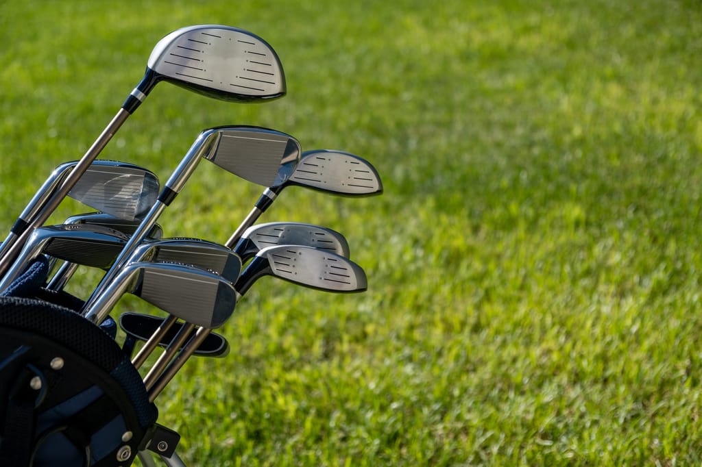 Golf club, sticks in a bag on green grass golf course background, close up view.