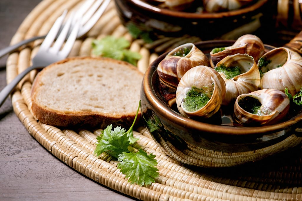 Escargots de Bourgogne - Snails with herbs butter, gourmet dish, in two traditional ceramic pans with coriander and bread on straw napkin. Close up