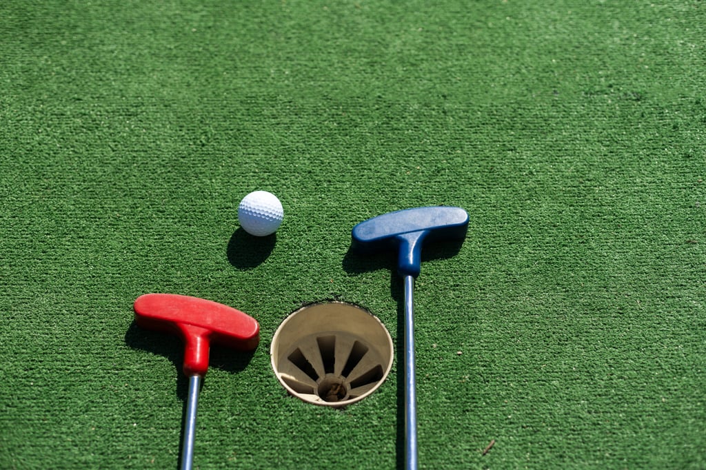 Close-up of miniature golf hole with bat and ball.