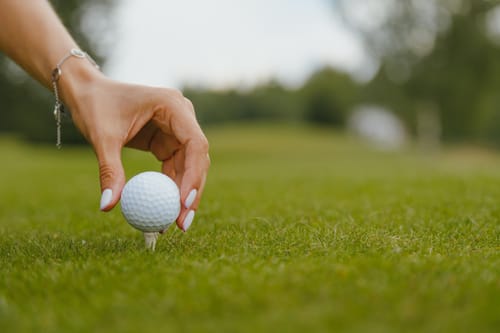 Woman's hand with a manicure puts a golf ball on a tee on a golf course. Female golfer without glove