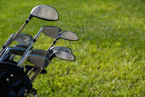 Golf club, sticks in a bag on green grass golf course background, close up view.